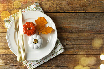 Autumn place setting, bokeh lights. Plate, cutlery and decor on wooden table, top view