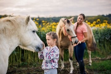 Girl gently stroking pony horse during calm moment with her mother and horses at family animal...
