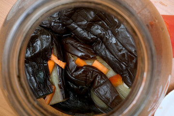 Colorful vegetables in a jar surrounded by dark leaves and spices