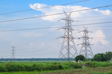 High voltage electric transmission tower with blue sky background. Electricity pylon in the green fields.