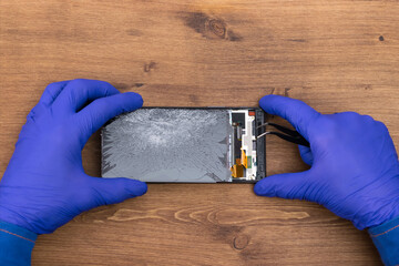 Hands of a craftsman repairing a broken phone display, close-up