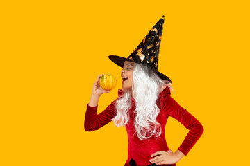 Halloween witch girl isolated on yellow. Pumpkin on Halloween. Witch All Hallows costume of girl. October 31 pumpkin. Costume party. Halloween pumpkin in hand of witch girl. Pumpkin spell