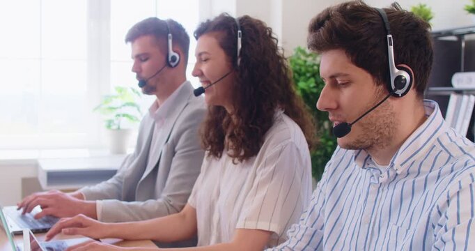 Help and assistance of call center agents team with headsets for customer calls. Group of operators with headphones typing and talking during work with hotline calls, responsive customer support - Powered by Adobe