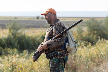 A hunter with a gun in camouflage clothing. A senior man with a gun, medium shot, searching for...