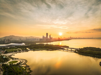 Aerial view of the modern city skyline with commercial buildings and green park along the bay at golden sunrise in Shenzhen.
