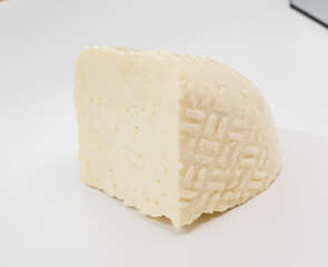A pale block of cheese with a soft, textured rind sits on a bright white surface