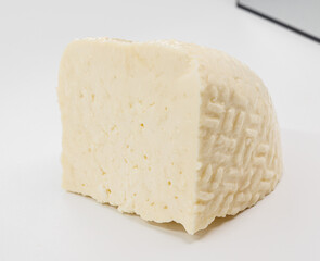A pale block of cheese with a soft, textured rind sits on a bright white surface