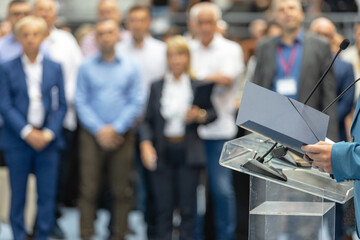 Business leader speaking at corporate conference with microphone and audience in background, professional speaker giving motivational presentation to group of business people