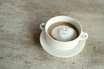 A cozy cup of coffee with creamy foam, offering warmth and comfort. The coffee sits on a saucer with two handles in a simple setting