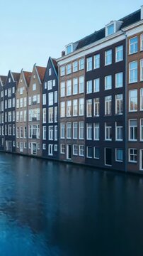 A row of buildings with a canal in between. The water is calm and reflects the buildings. The scene has a peaceful and serene mood