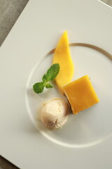 A refreshing mango dessert elegantly presented on a plate, featuring a scoop of ice cream and mint leaf