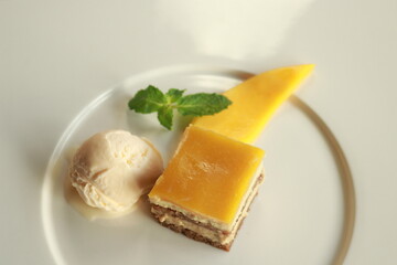 A beautifully plated dessert of cheesecake, mango, and ice cream on a white plate. This dessert offers a harmonious blend of textures and flavors