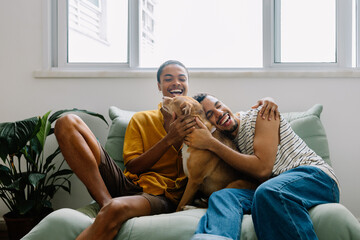Smiling couple cuddling caramel rescue dog on sofa at home