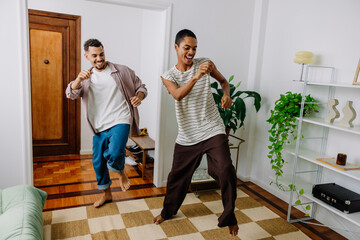 Gay couple dancing together in a living room with joyful expressions
