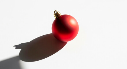 A festive, reflective red ornament casts a shadow on the bright white surface, embodying the essence of seasonal joy and decorative charm.