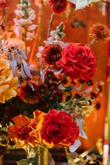 Close-up of rich autumn floral arrangement featuring vibrant yellow and deep red roses, chrysanthemums, and dry floral elements under warm, dramatic lighting