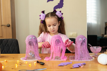 Young caucasian girl creating purple halloween decorations with glowing lights, Cheesecloth Ghosts,...