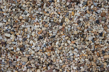 Textured gravel surface composed of various small stones in earthy tones, creating a natural landscape aesthetic ideal for backgrounds and design projects