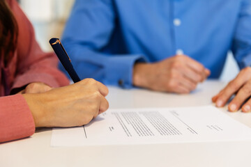 Close-up of a female hand signing an employment contract with a pen during a job interview meeting at the office. Recruitment, agreement, and career opportunity concept.