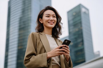 Asian young female professional holding smartphone in urban setting with skyscrapers