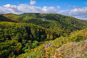 Panoramic view from Odvas-kő towards the Kemesnye Hill ridge in the Bükk Mountains, Hungary. Rolling autumn forest under a bright, cloudy sky.
