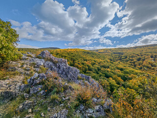 Panoramic autumn view from the limestone ridge of Odvas-kő in the Bükk Mountains, Hungary. Rolling hills covered in colorful forest under a vivid sky.