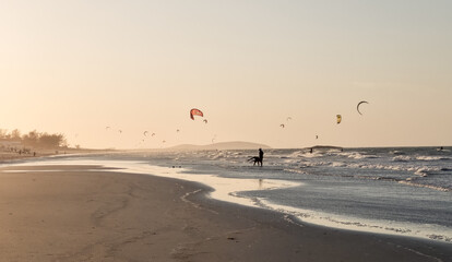 Evening kitesurfing session at golden hour, silhouettes riding waves while the sky glows. Tranquil...