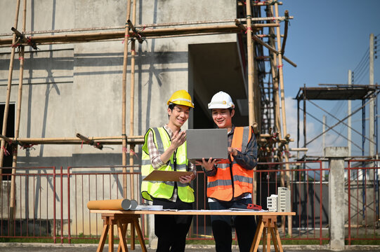 Construction supervisors discuss with a foreman about housing project progress while checking blueprints and data on a laptop