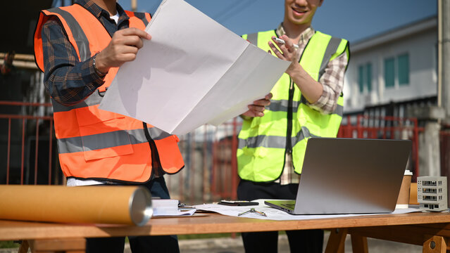 Close-up of two engineers collaborating on blueprint design and project data at a construction site