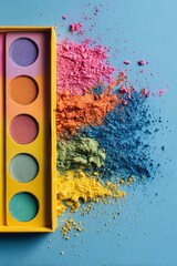 Brightly colored cosmetic powders are spilled next to an open makeup palette on a light blue surface