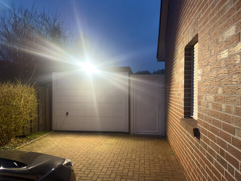 Ein heller Strahler leuchtet am Abend die Einfahrt zu einer Garage aus