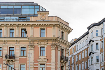 Intricate facades of classical urban buildings featuring decorative pilasters, ornate balconies, and modern glass rooftop extension under overcast sky