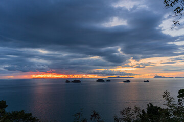 Wide View of Ocean with Small Islands under Dark Blue Clouds and Fiery Orange Horizon Light during Dusk, Tranquil Nature and Sunset Concept