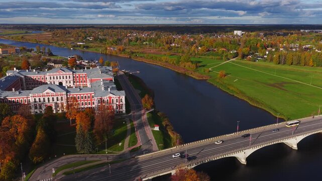 Aerial drone view of Jelgava Palace by the Lielupe River in Jelgava, Latvia. Late afternoon light, fall colors, bridge traffic, boats at a dock, lawns and paths.