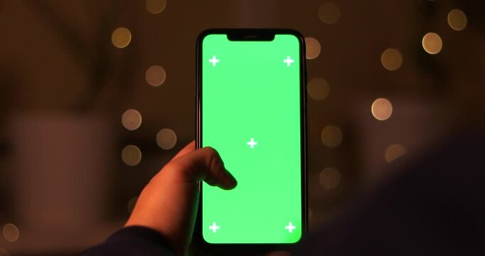 POV female hand holding smartphone with green screen chroma key near boke background, home atmosphere new year, Merry Christmas
