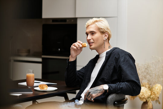 Young man enjoying a pastry and drink in a modern apartment setting during morning hours