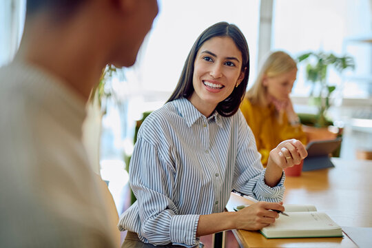 Young businesswoman smiling, listening, and engaging in conversation with a colleague in a bright office environment