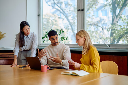 Professionals conducting a business meeting, actively collaborating and discussing documents while working on a laptop in a modern office