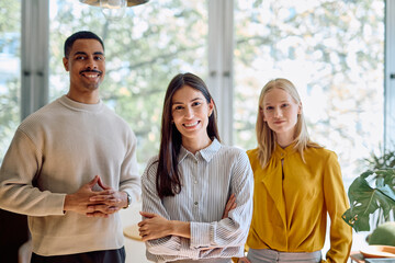 Diverse business team comprising a man and two women smiling, symbolizing successful collaboration and inclusion in a modern office