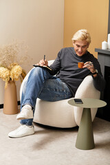 Young man enjoying coffee while sitting in a cozy apartment, capturing moments in a notebook