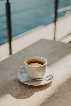 Cup of black coffee on a stone table in a cafe by the sea in a sunlight.