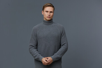 Male model in a cozy gray turtleneck sweater looking serious and contemplative, standing against a...