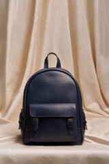 Deep blue leather rucksack stands centered against a draped pale fabric backdrop