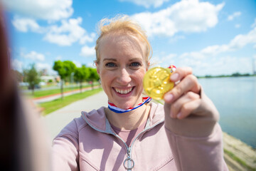 Woman smiling, celebrating victory, holding gold medal outdoors