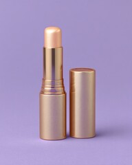 Gold-cased illuminating makeup stick product stands open against a solid lavender background
