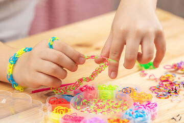 Child making colorful rubber band bracelets by hand on wooden table