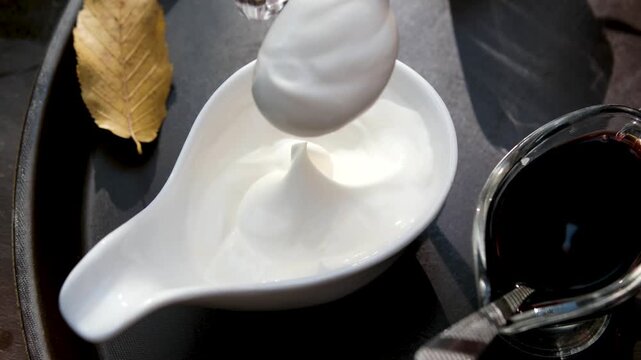 In a sauceboat, take out thick sour cream with a teaspoon and stir it on a plate. Autumn leaves, various sauces, autumn. High quality 4k footage