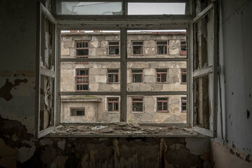 Cracked, peeling window frames look out onto derelict Soviet apartment building in Ugolnye Kopi, Chukotka, Russia, on a grey summer day.
