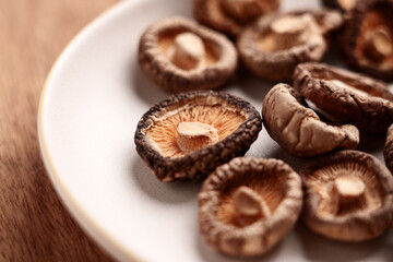 Dried shriveled edible shiitake mushrooms in ceramic bowl on wooden table. Dehydrated nutritious ingredient