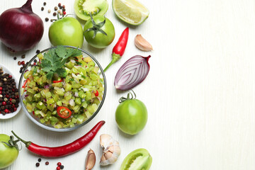 Tasty salsa in bowl and ingredients on white wooden table, flat lay. Space for text